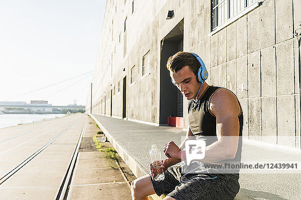 Young athlete wearing headphones  sitting on a wall  checking smartwatch