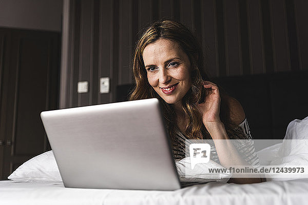 Smiling woman lying on bed at home looking at laptop