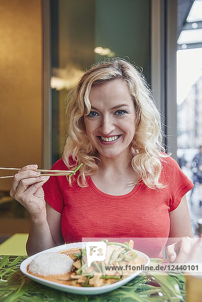 Portrait of smiling blond woman eating vegetarian Asian dish
