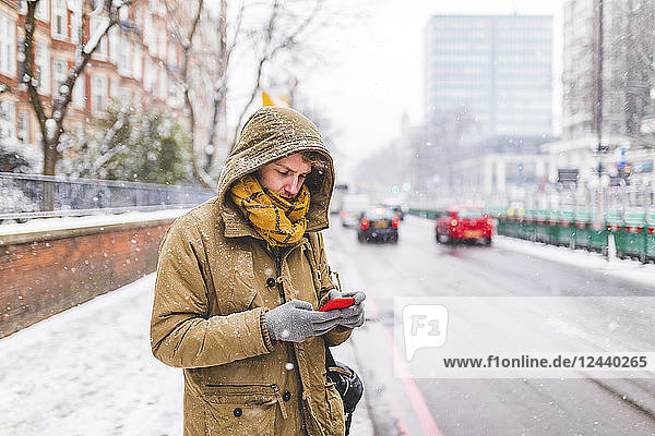 Young man standing next to the road in the city looking at cell phone