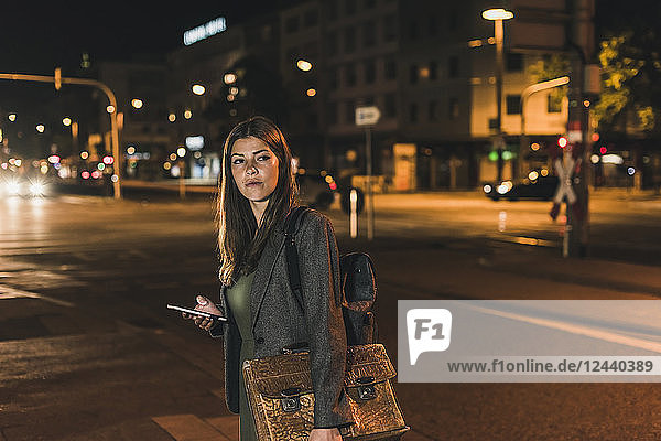 Portrait of young businesswoman with baggage and cell phone at night