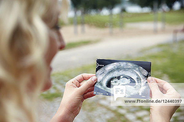 Pregnant woman looking at ultrasound image outdoors