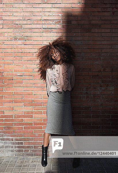 Portrait of beautiful young woman with afro hairdo at brick wall in sunshine