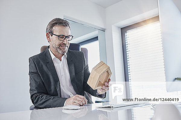 Smiling businessman at desk in office looking at architectural model