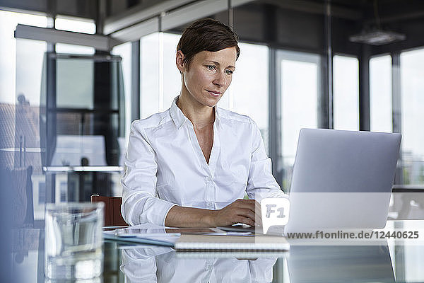 Businesswoman sitting at glass table in office using laptop
