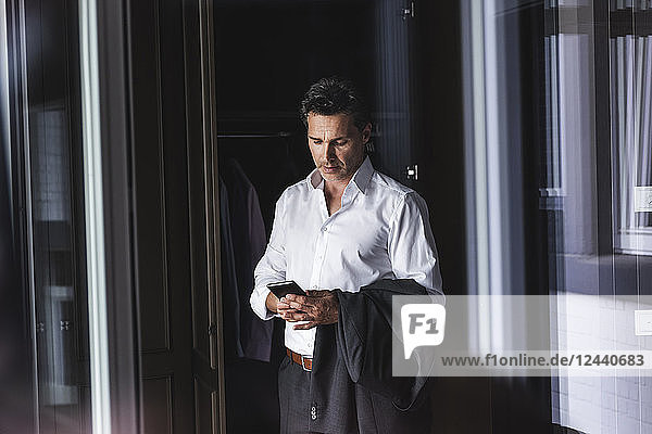 Businessman standing at wardrobe at home using cell phone