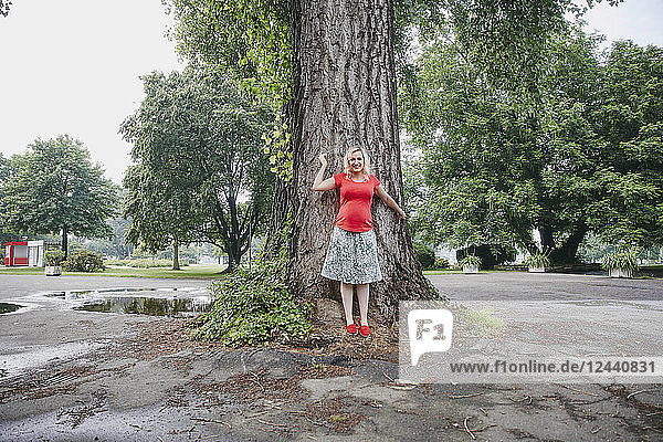 Portrait of smiling pregnant woman standing at a tree in park