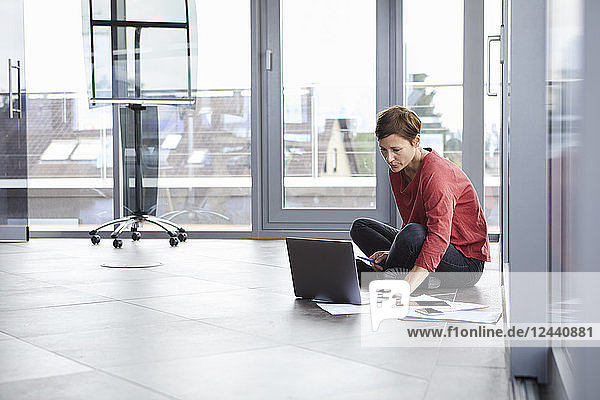 Businesswoman sitting on the floor in office using laptop