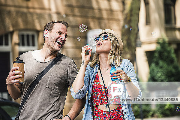 Happy couple with coffee to go blowing soap bubbles in the city