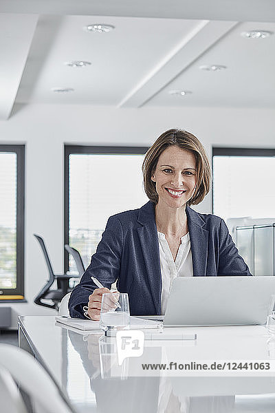 Portrait of smiling businesswoman using laptop at desk in office