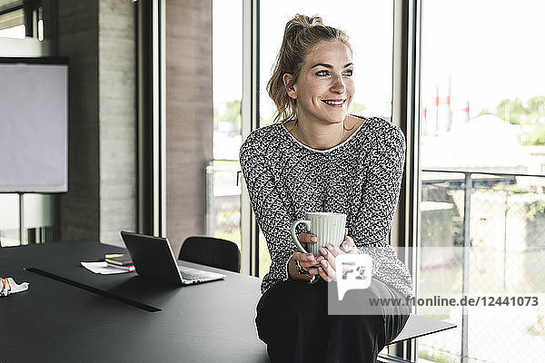 Young woman sitting in office  taking a break  drinking coffee