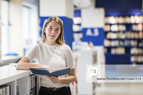 Portsrit of relaxed teenage girl with book in a public library