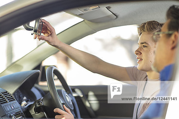 Learner driver with instructor in caradjusting rear view mirror