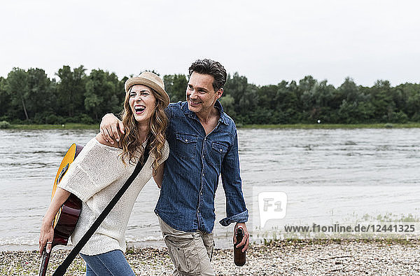 Happy couple walking at the riverside with beer bottle and guitar
