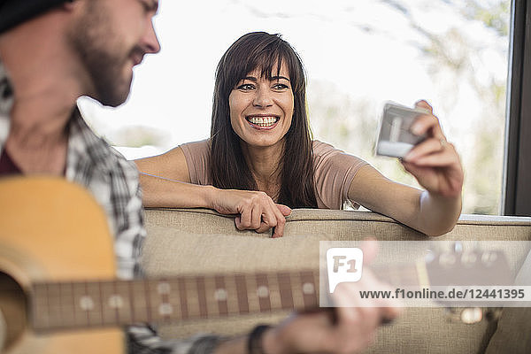 Young man at home playing guitar and woman taking a selfie