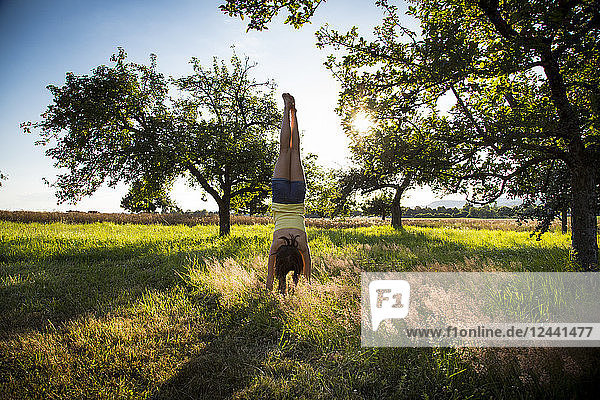 Young girl doing handstand on meadow at summer evening