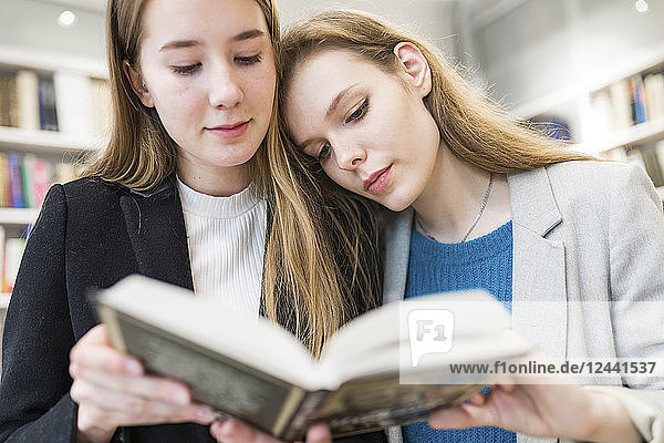 Portrait of two teenage girls reading booktogether in a public library
