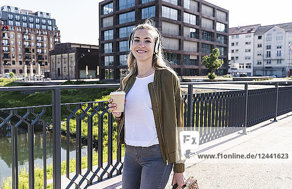 Young woman walking on bridge  drinking coffee  listening music with headphones