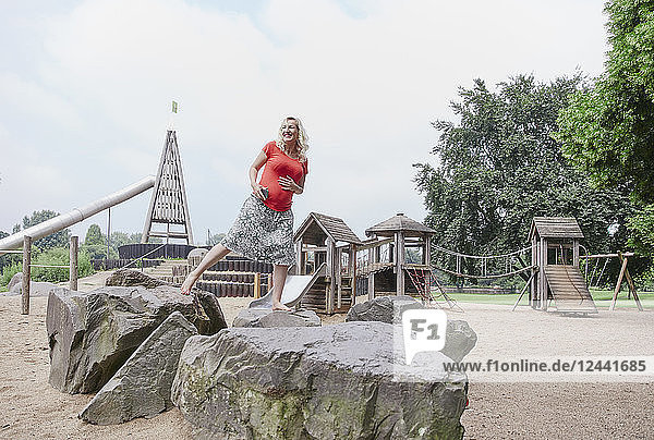 Happy pregnant woman balancing on a rock on playground