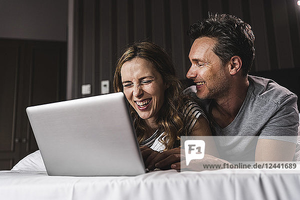 Happy couple lying on bed at home having fun with laptop