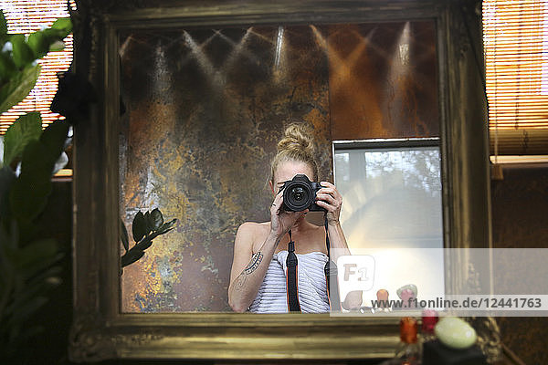 Mirror image of woman taking selfie with camera in bathroom