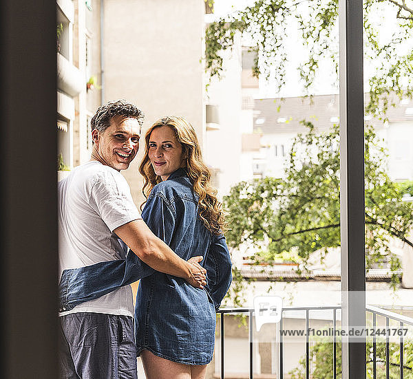 Happy couple in nightwear standing on balcony hugging
