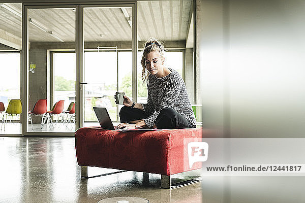 young businesswoman working in modern office  sitting on stool  using laptop
