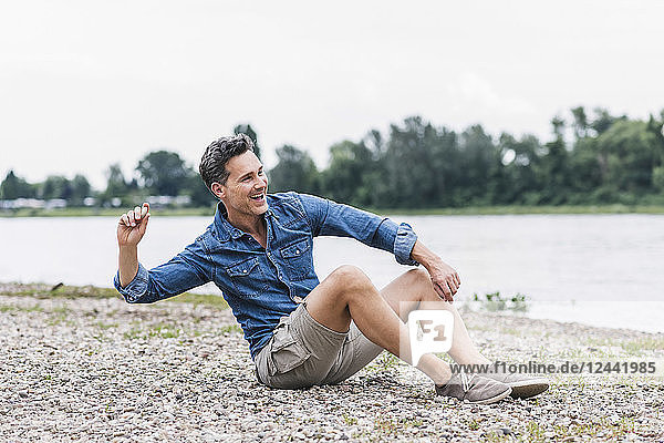 Laughing man sitting at the riverside throwing stones