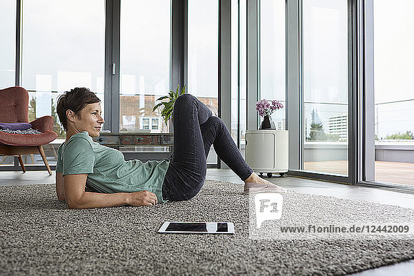 Woman lying on the floor at home with tablet looking out of balcony door