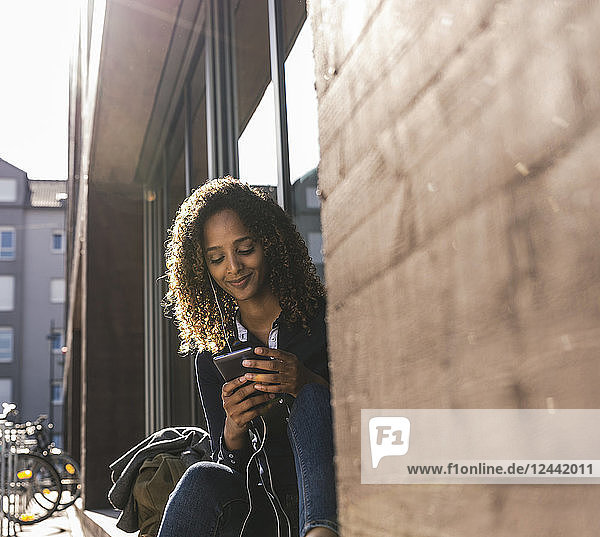 Young woman sitting in front of window in the city  using smartphone