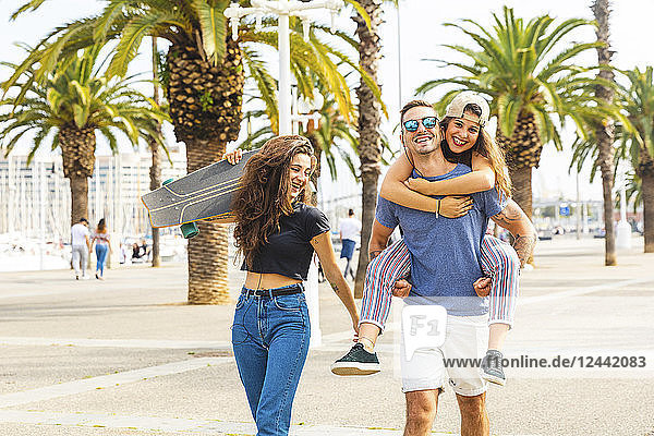 Happy friends with a skateboard walking on a promenade with palms