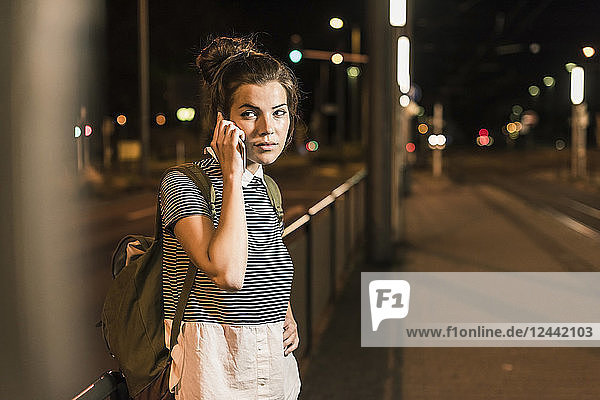 Portrait of young woman on the phone waiting at station by night