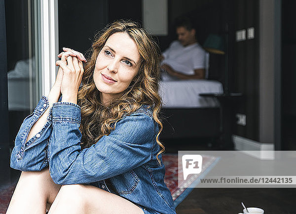 Smiling woman sitting at French window with man in background