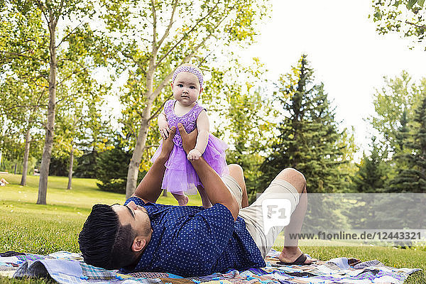 Ein Vater spielt mit seiner kleinen Tochter  während er auf einer Decke in einem Stadtpark im Spätsommer liegt; Edmonton  Alberta  Kanada