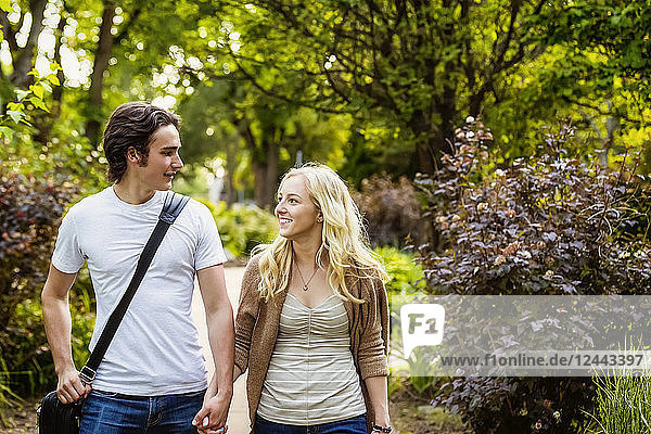 Ein junges Paar,  das händchenhaltend und redend einen Weg auf dem Universitätscampus entlanggeht,  Edmonton,  Alberta,  Kanada