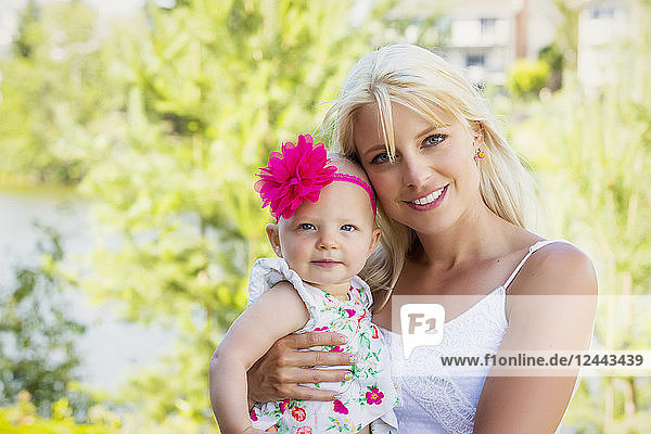 A beautiful young mother with long blonde hair enjoying quality time with her cute baby daughter in a city park on a summer day and posing for the camera  Edmonton  Alberta  Canada