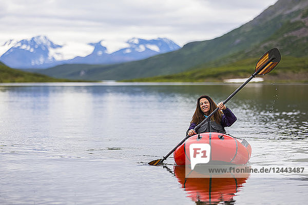 Eine Frau paddelt mit einem Packraft über den Landmark Gap Lake  abseits des Denali Highway  mit der Alaska Range in der Ferne  Alaska  Vereinigte Staaten von Amerika