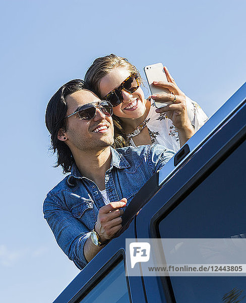 Ein junges Paar steht durch das Schiebedach seines Autos auf und macht ein Selbstporträt mit seinem Handy  Edmonton  Alberta  Kanada