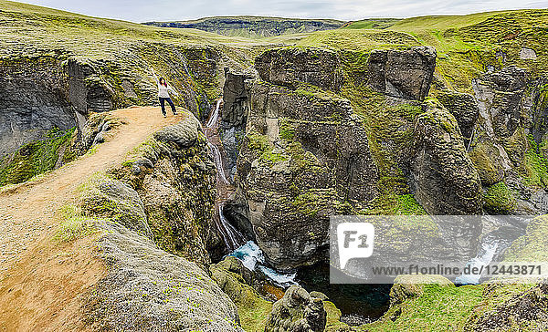 Eine Touristin steht an einem Aussichtspunkt auf einer Klippe im malerischen Tal von Fjadrargljufur in Südisland,  Island