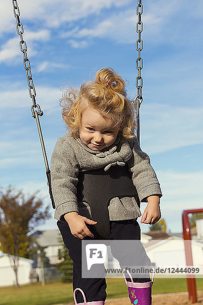 Ein niedliches junges Mädchen  das mit einem lustigen Gesicht nach unten schaut  während es auf einem Spielplatz während der Herbstsaison schaukelt  Spruce Grove  Alberta  Kanada