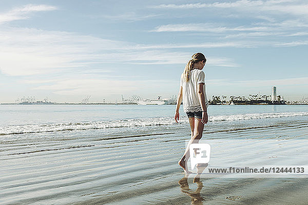 A girl walking on the beach on the wet sand; Long Beach  California  United States of America