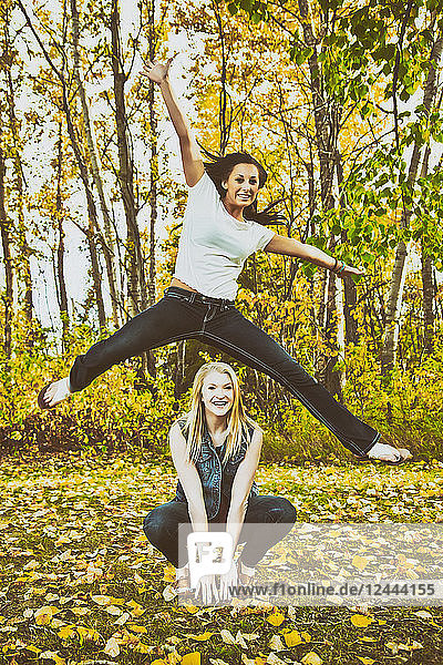 Eine junge Frau springt hoch in die Luft über ihre Freundin in einem Park während der Herbstsaison  Edmonton  Alberta  Kanada