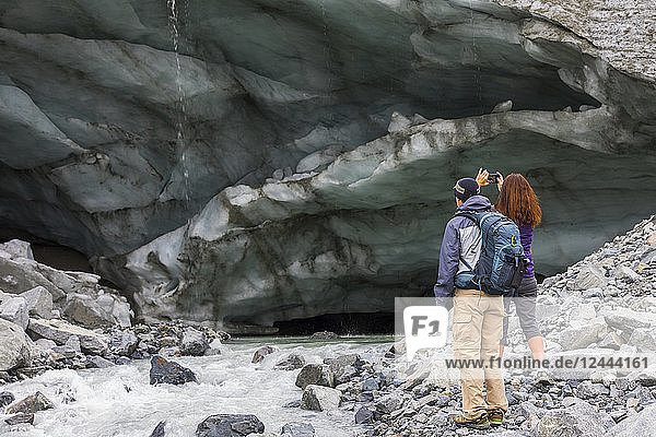 A woman takes a photograph of an ice cave with her cell phone while hiking to Gulkana Glacier with her husband  Alaska  United States of America