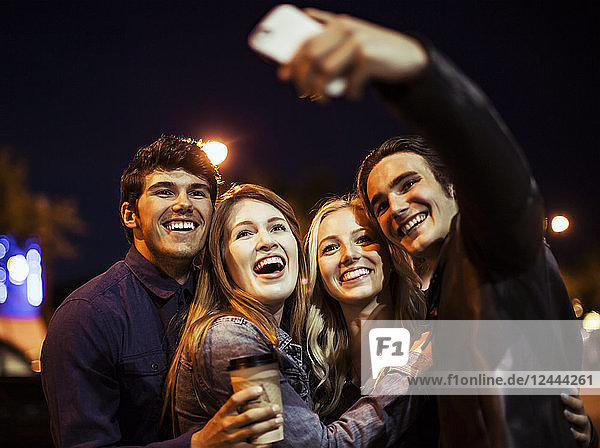 Zwei junge Paare stehen nachts auf der Straße eng beieinander und posieren für ein Selbstporträt mit einem Smartphone  Edmonton  Alberta  Kanada
