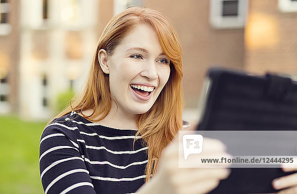 Eine junge Frau mit roten Haaren lächelt breit,  während sie auf ein Tablet schaut,  Edmonton,  Alberta,  Kanada