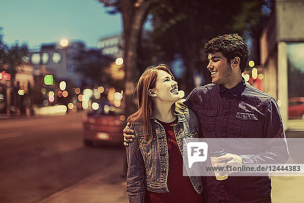 Ein junges Paar geht in der Abenddämmerung einen Bürgersteig in einem beliebten Szeneviertel entlang  Edmonton  Alberta  Kanada