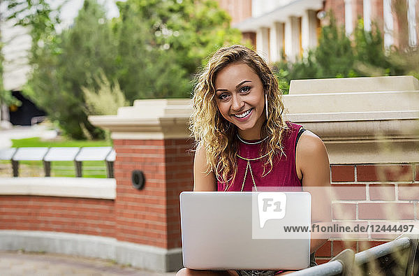 Porträt einer schönen jungen Studentin  die draußen auf dem Campus ihren Laptop benutzt  Edmonton  Alberta  Kanada