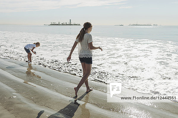 Two sisters walking out to the surf on a beach; Long Beach  California  United States of America