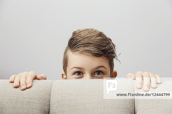 Porträt eines kleinen Jungen  der hinter einer Couch hervorschaut und in die Kamera schaut; Langley  British Columbia  Kanada