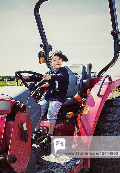 Ein kleiner Junge  der mit schief sitzendem Hut auf einem roten Traktor auf einer Farm fährt  Edmonton  Alberta  Kanada